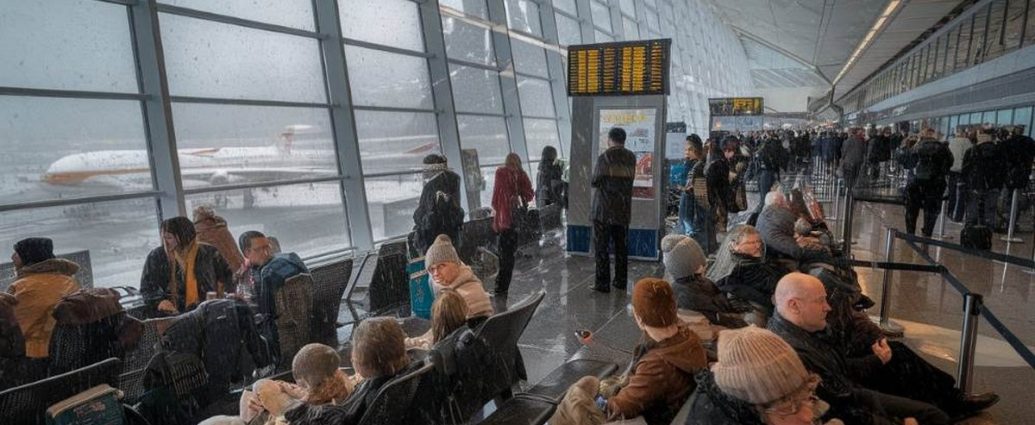 flight delays Canada - Snow-covered aircraft and airport runway during winter storm causing flight delays